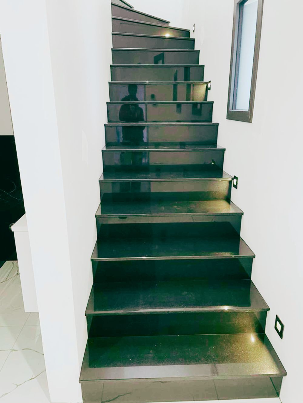 : Escalier intérieur moderne avec marches en finition noire brillante et éclairage mural – Pose et rénovation AK dans le Pays de Gex